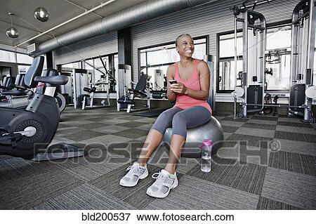 Stock Photo - African American woman text messaging on cell phone in health club. Fotosearch