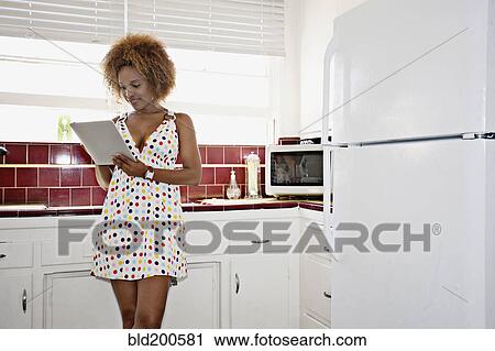 Stock Image - African American woman using digital tablet in kitchen. Fotosearch