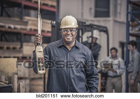 Stock Image - African American worker holding control panel in factory. Fotosearch