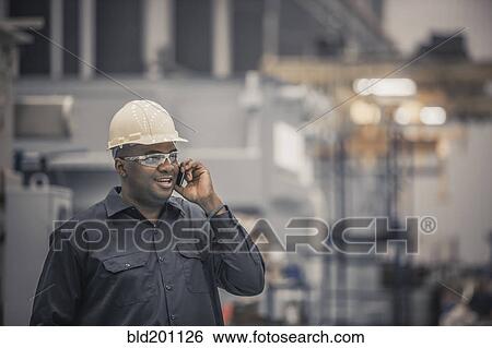 Stock Photograph - African American worker using cell phone in factory. Fotosearch