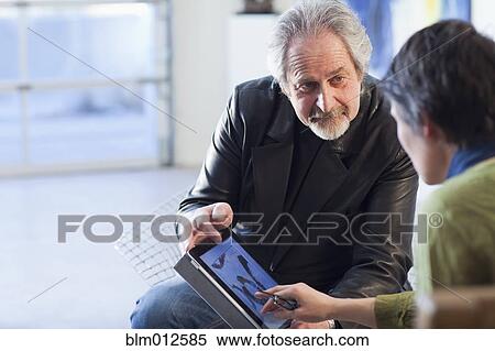 Stock Photography - Art gallery curator using digital tablet with customer. Fotosearch