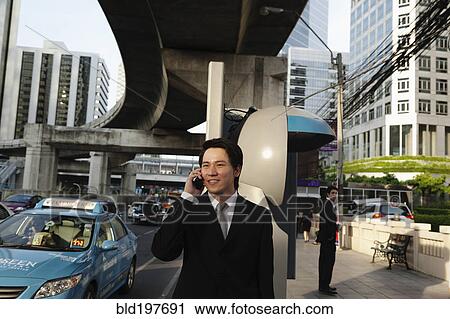Stock Image - Asian businessman talking on cell phone outdoors. Fotosearch