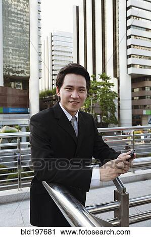 Stock Image - Asian businessman text messaging on cell phone outdoors. Fotosearch