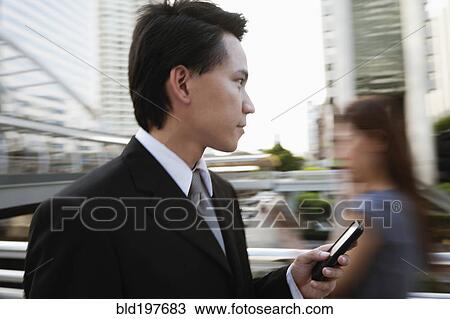 Stock Image - Asian businessman text messaging on cell phone outdoors. Fotosearch