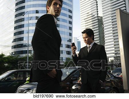 Stock Image - Asian businessman text messaging on cell phone outdoors. Fotosearch