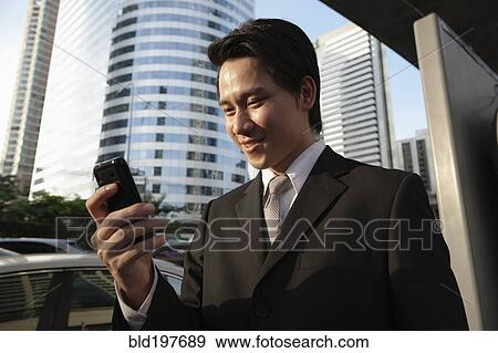 Asian businessman text messaging on cell phone outdoors View Large Photo Image Stock Photo - Asian businessman text messaging on cell phone outdoors. Fotosearch
