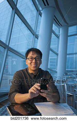 Stock Photograph - Asian businessman text messaging on cell phone. Fotosearch