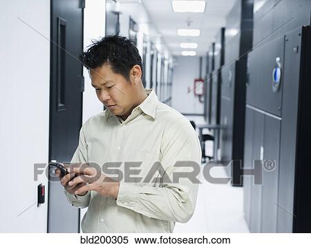 Stock Photography - Asian businessman using cell phone in server room. Fotosearch