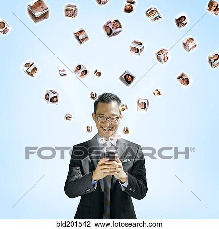 Stock Image - Asian businessman using cell phone with images floating above. Fotosearch
