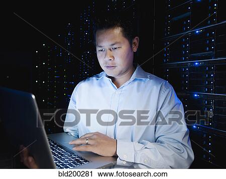 Stock Image - Asian businessman working in server room. Fotosearch