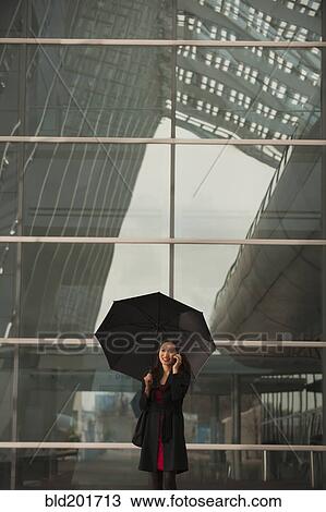 Stock Image - Asian businesswoman with umbrella talking on cell phone. Fotosearch