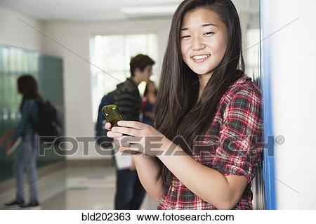Stock Image - Asian high school student text messaging on cell phone. Fotosearch