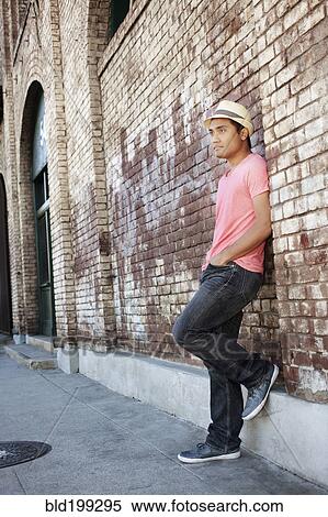 Stock Photography - Asian man leaning against brick wall. Fotosearch