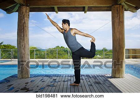 Stock Image - Asian man practicing yoga at poolside. Fotosearch