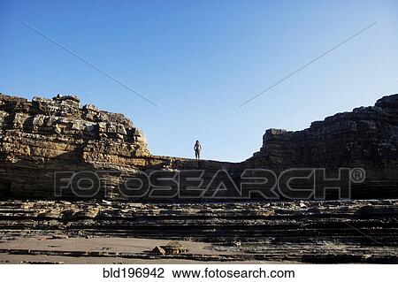 Stock Image - Asian man standing on cliff's edge. Fotosearch