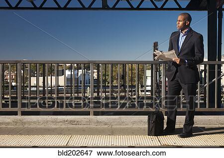 Black businessman reading newspaper and waiting at train station View Large Photo Image Stock Photo - Black businessman reading newspaper and waiting at train station. Fotosearch
