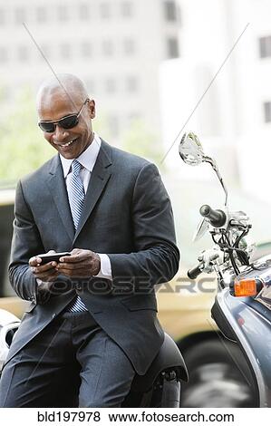 Stock Photo - Black businessman sitting on scooter text messaging. Fotosearch