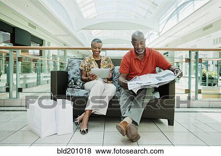 Stock Photo - Black couple relaxing on sofa in shopping mall. Fotosearch