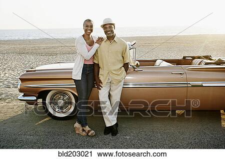 Stock Image - Black couple standing by convertible. Fotosearch