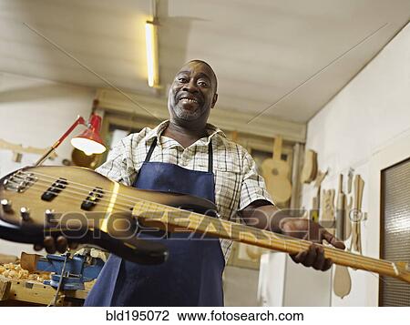 Stock Image - Black craftsman holding electric guitar in workshop. Fotosearch