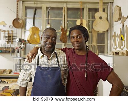 Stock Photo - Black craftsman in guitar workshop with son. Fotosearch