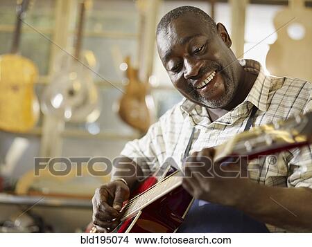 Black craftsman playing guitar in workshop View Large Photo Image Picture - Black craftsman playing guitar in workshop. Fotosearch