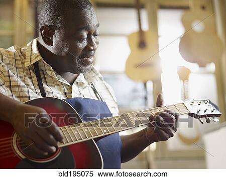 Stock Photography - Black craftsman playing guitar in workshop. Fotosearch