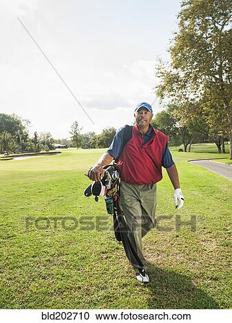 Stock Image - Black man carrying golf clubs. Fotosearch