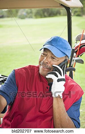 Stock Photo - Black man on cell phone in golf cart. Fotosearch