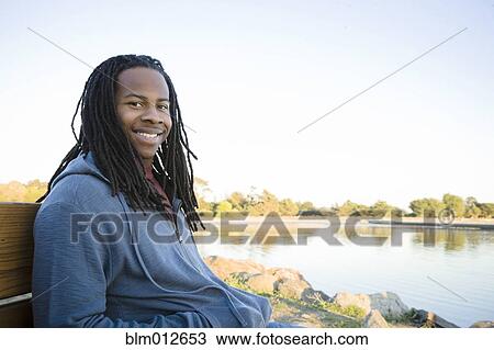 Stock Image - Black man sitting near shore. Fotosearch