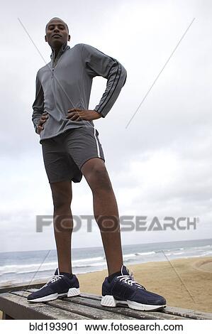 Stock Image - Black man standing on bench at beach. Fotosearch