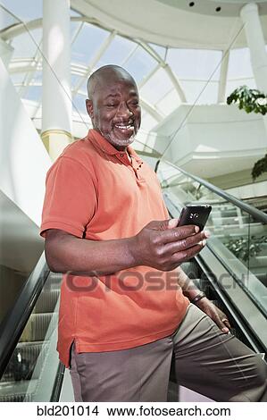 Picture - Black man text messaging on mall escalator. Fotosearch