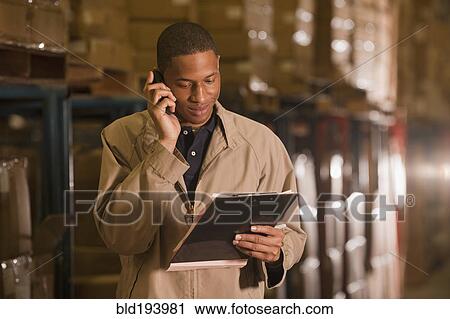 Stock Image - Black man working in warehouse and talking on cell phone. Fotosearch