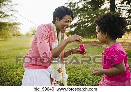 Black mother and daughter blowing bubbles in park View Large Photo Image Stock Photo - Black mother and daughter blowing bubbles in park. Fotosearch