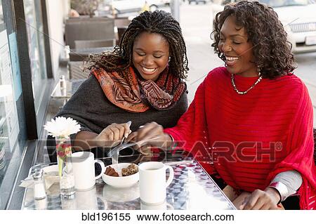 Stock Photography - Black mother and daughter having coffee at outdoor cafe. Fotosearch