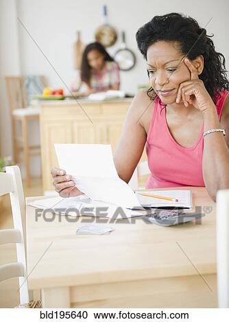 Stock Image - Black mother looking at monthly bills. Fotosearch