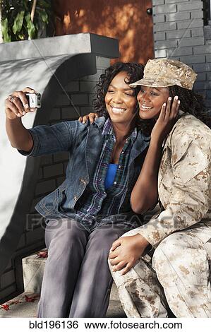 Stock Photograph - Black mother taking self-portrait with soldier daughter. Fotosearch