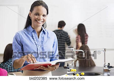Stock Photography - Black teacher holding book in classroom. Fotosearch