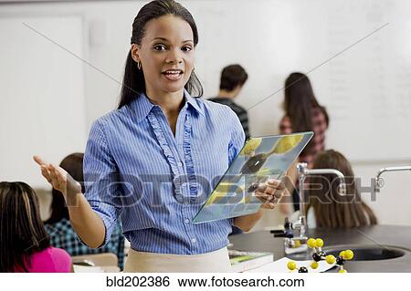 Stock Photograph - Black teacher holding digital tablet in classroom. Fotosearch