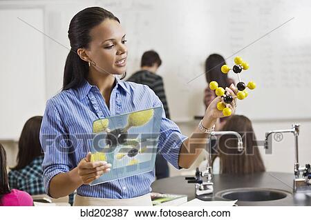 Stock Photo - Black teacher holding digital tablet and chemistry model in classroom. Fotosearch