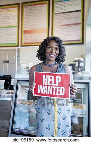 Stock Photo - Black woman holding help wanted sign in bakery. Fotosearch