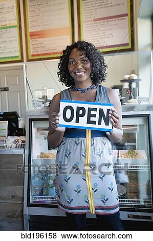 Black woman holding open sign in bakery View Large Photo Image Stock Photo - Black woman holding open sign in bakery. Fotosearch
