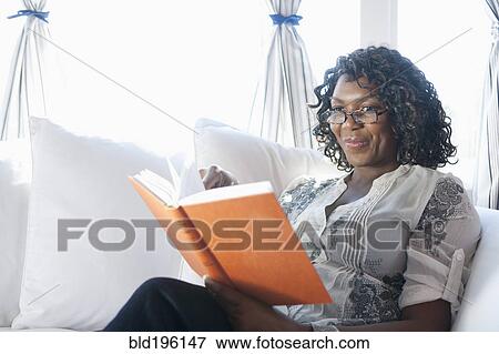 Stock Photo - Black woman reading book on sofa. Fotosearch