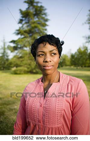 Stock Image - Black woman standing in park. Fotosearch