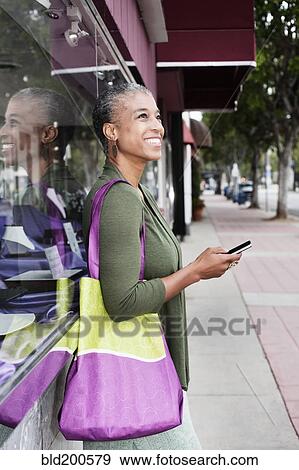 Stock Photo - Black woman text messaging on sidewalk. Fotosearch