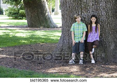 Boy and girl leaning against tree trunk in park View Large Photo Image Stock Photography - Boy and girl leaning against tree trunk in park. Fotosearch