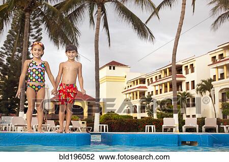 Stock Image - Brother and sister standing at resort poolside holding hands. Fotosearch
