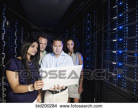 Picture - Business people looking at laptop in server room. Fotosearch