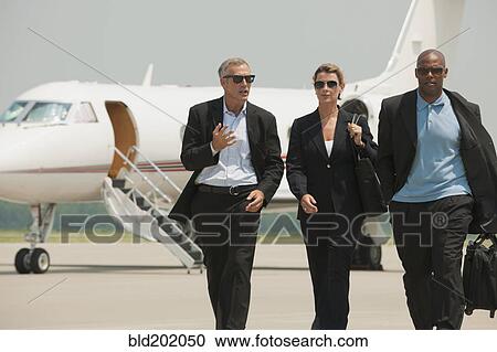 Stock Image - Business people walking on airport tarmac. Fotosearch