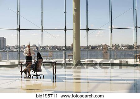 Stock Image - Business people working in large office with glass wall. Fotosearch